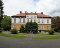 Zdjęcie przedstawia pałac w Zieleninie. Na pierwszym planie widać frontową elewację, która częściowo przysłonięta jest przez zieleń.                                                                    