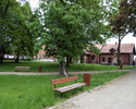 Zdjęcie przedstawia park w Troszynie. Na pierwszym planie widać aleję spacerową. W tle widoczny jest fragment zabudowań dawnego folwarku.                                                               