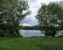 Zdjęcie przedstawia park w Przyjezierzu. Na pierwszym planie widać brzeg, dalej drzewa i jezioro.                                                                                                       