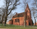 Zdjęcie przedstawia stronę wejścia oraz stronę boczną kościoła, który został wykonany z czerwonej cegły.                                                                                                