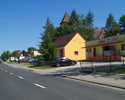 Zdjęcie przedstawia główną drogę we wsi Postomino wraz z zabudowaniami.                                                                                                                                 