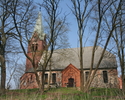 Zdjęcie przedstawia boczną stronę kościoła wykonanego z czerwonej cegły. Usytuowany na lekkim wzniesieniu.                                                                                              