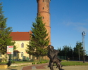 Zdjęcie przedstawia latarnię morską w Jarosławcu wraz z pomnikiem rybaka.                                                                                                                               