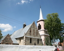 Zdjęcie przedstawia stronę wejścia kościoła zbudowanego z kamienia. Kościół ogrodzony wysokim białym murem.                                                                                             