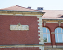 Zdjęcie przedstawia fragment budynku rektoratu US. Na pierwszym planie widać skrzydło, na którym widoczna jest inskrypcja w języku łacińskim.                                                           