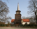 Zdjęcie przedstawia stronę wejścia kościoła, którego wieża wykonana została z drewna.Kościół usytuowany na lekkim wzniesieniu.                                                                          