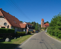 Zdjęcie przedstawia drogę wraz z zabudowaniami przebiegającą przez wieś Sławsko. Na końcu drogi widoczny jest kościół.                                                                                  