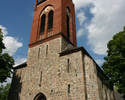 Zdjęcie przedstawia kościół od strony wejścia, którego wieża zbudowana jest z czerwonej cegły .                                                                                                         