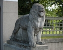 Zdjęcie przedstawia Pałac pod Lwami. Na pierwszym planie widać rzeźbę lewa, która stoi przed bramą wejściową na teren wokół pałacu.                                                                     