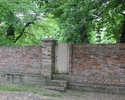 Zdjęcie przedstawia park w Lubiechowie Górnym. Na pierwszym planie widać mur otaczający park i furtkę, która do niego prowadzi.                                                                         