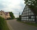 Zdjęcie przedstawia fragment głównej drogi we wsi Marszewo wraz z zabudowaniami.                                                                                                                        