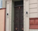 Zdjęcie przedstawia kamienicę  przy ul. Kościuszki w Trzcińsku-Zdroju. Na pierwszym planie widać zdobione drzwi wejściowe do budynku.                                                                   
