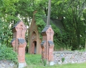 Zdjęcie przedstawia mauzoleum w Chełmie Dolnym. Na pierwszym planie widać bramę w cmentarnym murze, która prowadzi do mauzoleum, w tle zabytek pośród drzew.                                            