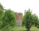 Zdjęcie przedstawia basztę prochową w Baniach. Na pierwszym planie widać drzewa otaczające zabytek, pomiędzy nimi budowla.                                                                              