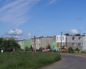Zdjęcie przedstawia główną drogę we wsi Pieszcz wraz z budynkami mieszkalnymi.                                                                                                                          