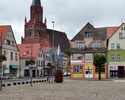Zdjęcie przedstawia plac oraz budynki sąsiadujące które znajdują się na Terenie Starego Miasta oraz kościół widoczny w oddali                                                                           
