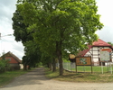 Zdjęcie przedstawia drogę wraz z zabudowaniami w miejscowości Pomiłowo. Z prawej strony drogi umieszczone są tablice informującę o regionie i ścieżce rowerowej.                                        