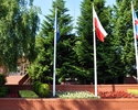 Zdjęcie trzech masztów z flagami witających podróżnych zmierzających do urzędu gminy, z wejściem widzianym w tle                                                                                        