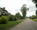 Zdjęcie przedstawia drogę we wsi Janiewice wraz z zabudowaniami.                                                                                                                                        