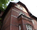 Zdjęcie przedstawia górną część budynku z czerwonej cegły.                                                                                                                                              
