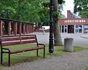 zdjęcie przedstawia ławkę ulokowaną na terenie dworca oraz jego budynek główny w tle                                                                                                                    