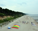 Zdjęcie wykonane z platformy widokowej, przedstawia plażę wraz z brzegiem klifowym, morzem oraz dmuchańcem do skakania dla dzieci                                                                       