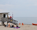 zdjęcie przedstawia budkę ratowniczą na piaszczystej plaży wraz z ratownikami oraz turystami                                                                                                            