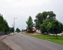 zdjęcie przedstawia przystanek autobusowy, ulicę przy której się znajduje, w tle, po prawej stronie, widać również stację kolei wąskotorowej                                                            