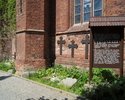 Zdjęcie przedstawia fragment lapidarium przy kościele pw. Matki Bożej Częstochowskiej w Darłowie wraz z tablicą informacyjną.                                                                           