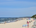 Zdjęcie przedstawia piaszczystą plaże, kamienny brzeg klifowy, morze oraz wypoczywających turystów                                                                                                      