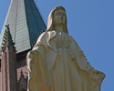 Zdjęcie przedstawia figurę Matki Boskiej na tle wieży kościoła PW NMP w Połczynie-Zdroju.                                                                                                               