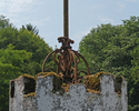 Zdjęcie przedstawia zbliżenie na jedną z wieżyczek na murze  otaczającym dworek w Paszęcinie, przy drodze wjazdowej do miejscowości.  W tle park dworski.                                               