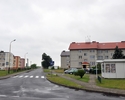 Zdjęcie przedstawia skrzyżowanie w Prusinowie, sklep, bloki mieszkalne oraz przystanek autobusowy w dali.                                                                                               