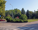 Zdjęcie przedstawia Plac 1000-lecia w Połczynie -Zdroju, fragment z małym parkiem w centrum placu. Po lewej i prawej przystanki autobusowe.                                                             