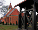 Zdjęcie przedstawia kościół z czerwonej cegły i drewnianą wieżę.                                                                                                                                        