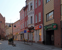 Zdjęcie przedstawia budynki przy ulicy 1 Maja, bankomat, aptekę, przychodnię i fragment bramy miejskiej w Świdwinie,  widok od strony Placu Jana Pawła II.                                              