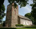 Zdjęcie przedstawia stronę wejścia oraz ścianę boczna kościoła zbudowanego z kamienia.                                                                                                                  