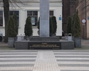 Widok na pomnik w formie obelisku, sąsiednie budynki oraz fragment Placu Zwycięstwa.                                                                                                                    