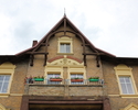 Zdjęcie przedstawia dom przy ul. Grunwaldzkiej 4 w Widuchowej. Na pierwszym planie widać drewniane elementy w górnej części budynku oraz dwa balkony w centralnej części elewacji frontowej.            