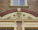 Zdjęcie przedstawia fragment elewacji domu przy ul. Grunwaldzkiej 4 w Widuchowej. Na pierwszym planie widoczna jest górna część elewacji frontowej z ujęciem drewnianych ozdób, które znajdują się pod d