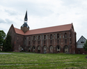 Zdjęcie przedstawia jeden z budynków, który wchodzi w skład dawnego klasztoru cystersów w Kołbaczu. Na pierwszym planie widoczna jest boczna elewacja kościoła.                                         