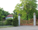 Zdjęcie przedstawia pałac w Chełmie Górnym. Na pierwszym planie widać bramę wjazdową na teren przy pałacu, w tle, po lewej stronie zabytek.                                                             