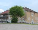 Zdjęcie przedstawia budynek z dawnego folwarku w Gogolicach. Na pierwszym planie widać fragment podwórza gospodarczego, w tle pałac, który jest częściowo przysłonięty drzewem.                         