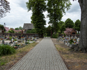 Zdjęcie przedstawia cmentarz przykościelny w Troszynie. Na pierwszym planie widać aleję, która przebiega przez teren nekropolii.                                                                        