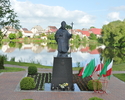 Zdjęcie przedstawia pomnik Jana Pawła II na tle panoramy  miasta z jeziorem.                                                                                                                            