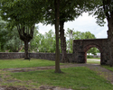 Zdjęcie przedstawia cmentarz przykościelny w Mirowie. Na pierwszym planie widać bramę prowadzącą na teren kościoła, po lewej stronie, w tle żeliwny krzyż.                                              