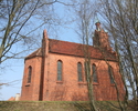 Zdjęcie przedstawia boczną ścianę oraz tył kościoła, który wykonany został z czerwonej cegły i usytuowany jest na wzniesieniu.                                                                          
