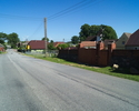 Zdjęcie przedstawia główną drogę we wsi Chudaczewo wraz z zabudowaniami.                                                                                                                                