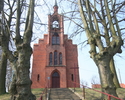 Zdjęcie przedstawia stronę wejścia kościoła, który wykonany został z czerwonej cegły i usytuowany jest na wzniesieniu.                                                                                  