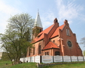 Zdjęcie przedstawia boczną ścianę oraz tył kościoła zbudowanego z czerwonej cegły, usytuowanego na wzniesieniu. Kościół ogrodzony jest białym murowanym płotem.                                         